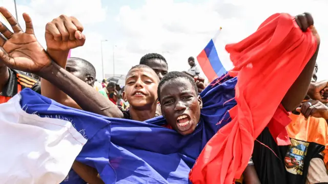 Un homme recouvert d'un drapeau russe agite les bras et crie alors que les partisans des chefs militaires du Niger se rassemblent pour manifester devant les bases aériennes nigériennes et françaises à Niamey, le 27 août 2023.